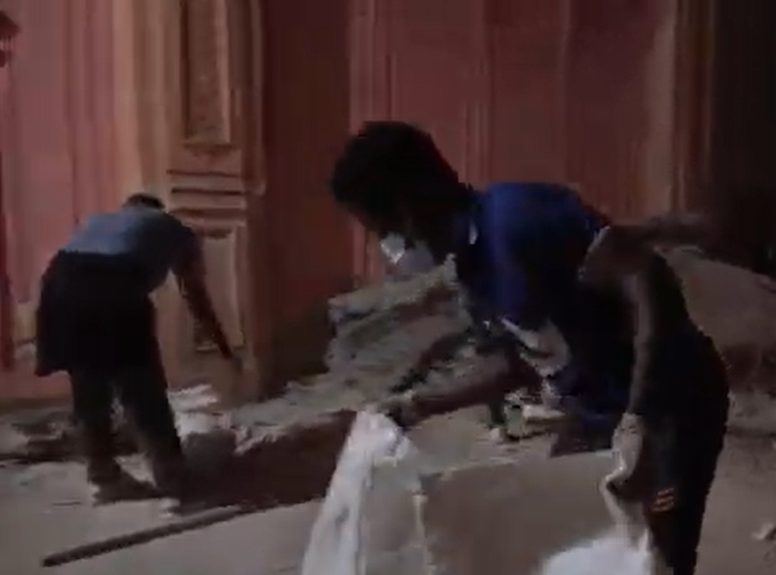 Two people clearing rubble from the floor of Le Colisée's hall, in front of the old stage curtains